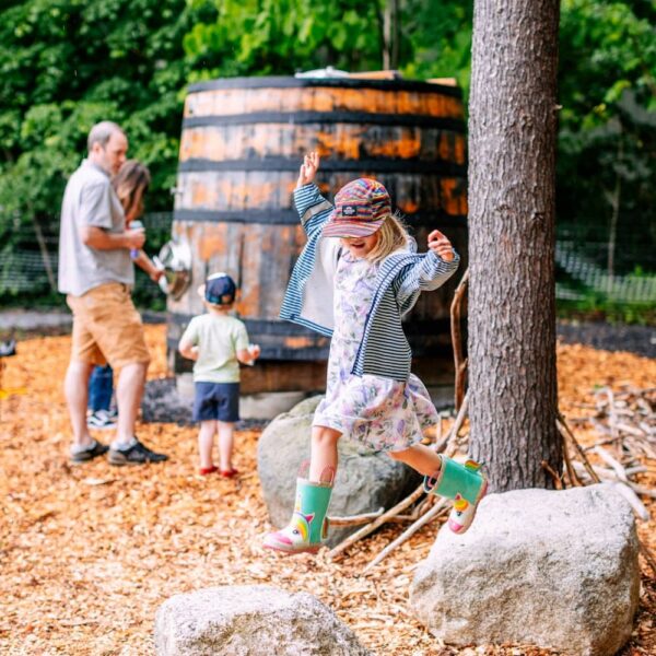 Allagash Backyard Opening Day_Ask to use please (5 of 65) (2) (1) A little girl jumps between two rocks in the Backyard area at Allagash Brewing Company