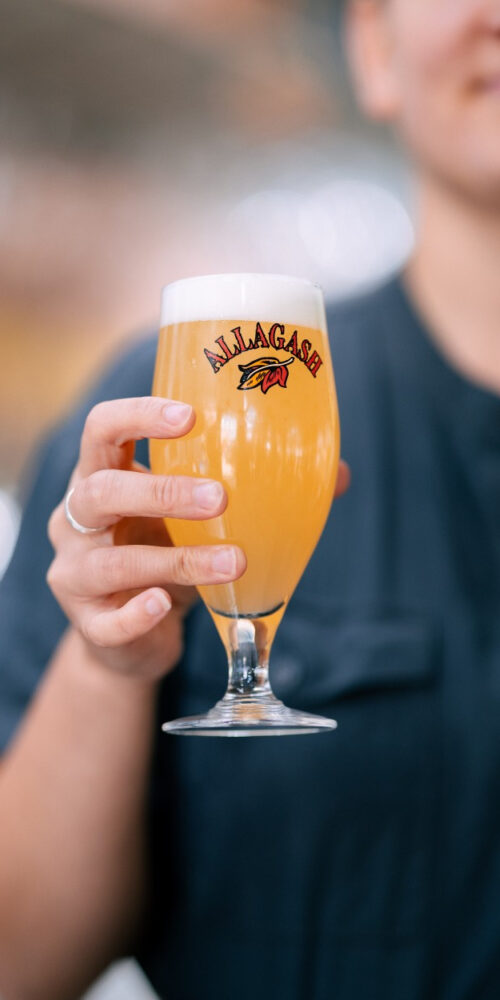 Woman holds up a chalice of beer in the Allagash Tasting Room