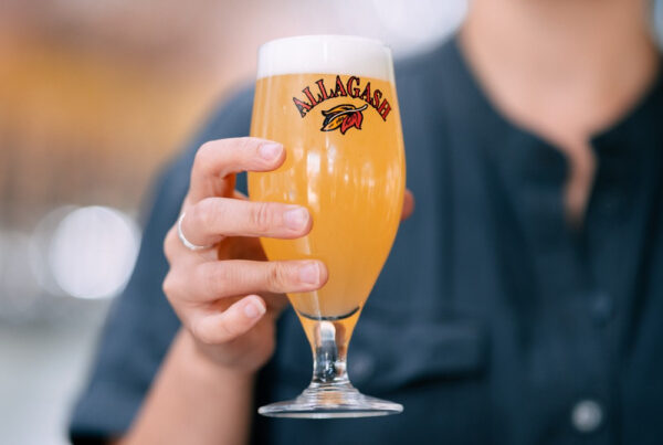Woman holds up a chalice of beer in the Allagash Tasting Room