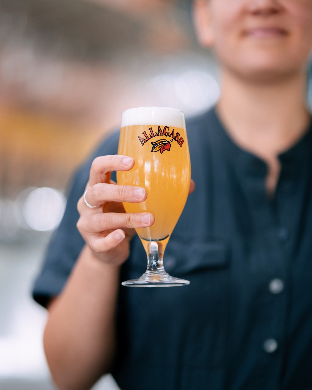 Woman holds up a chalice of beer in the Allagash Tasting Room